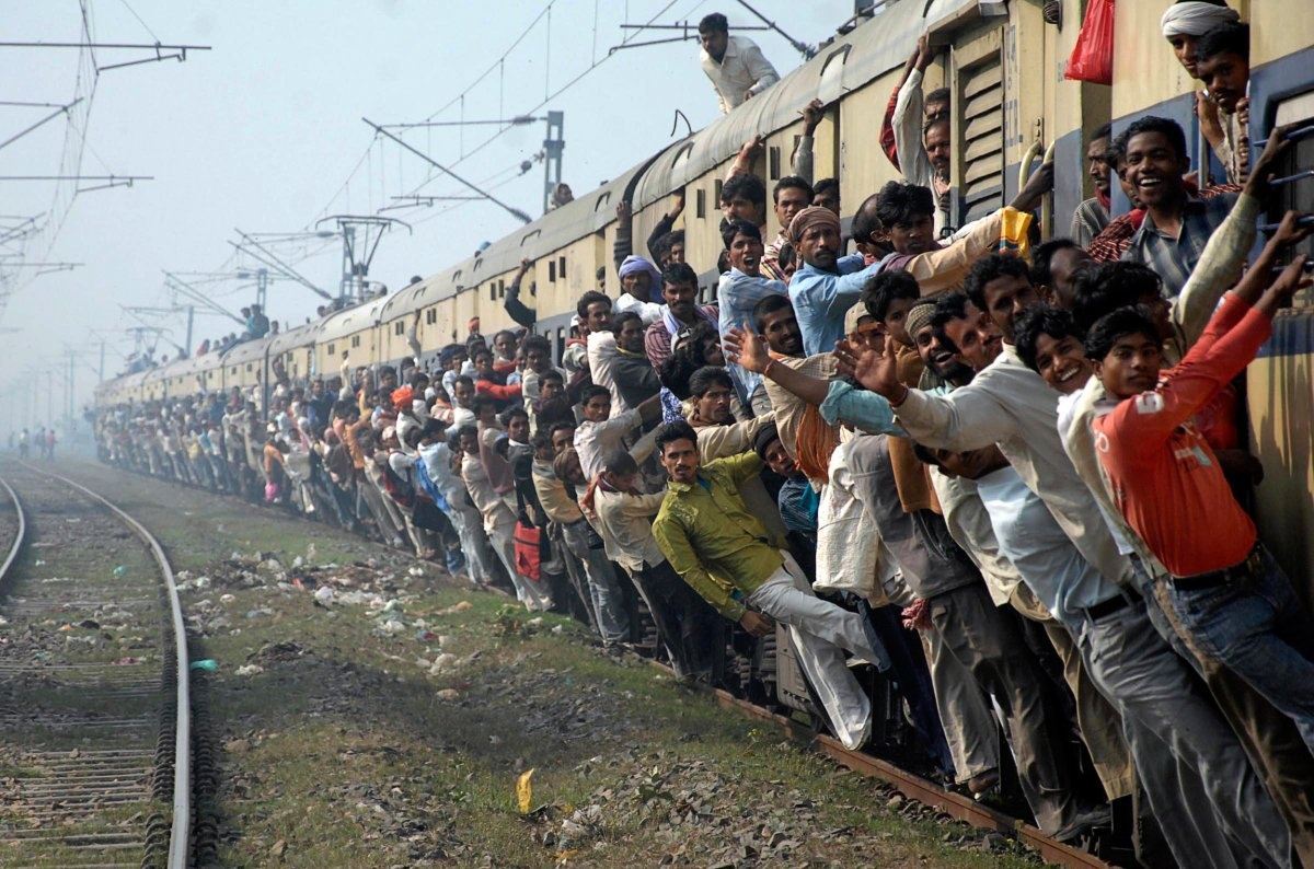 Young men ride packed onto the sides and roof of an overcrowded passenger train in India.